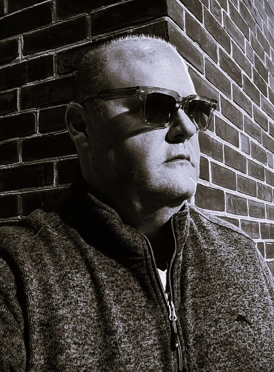 WitheringWithout (Withering Without) in sunglasses against a brick wall, black and white portrait